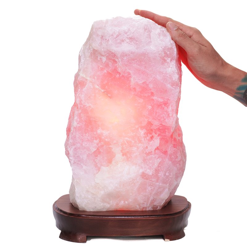 Pink quartz lamp with soft rose hue on dark wooden base.