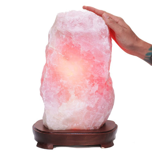Pink quartz lamp with soft rose hue on dark wooden base.