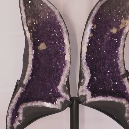 Geode angel wings formed from a split amethyst geode on metal display stand.