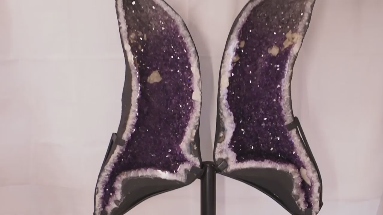 Geode angel wings formed from a split amethyst geode on metal display stand.